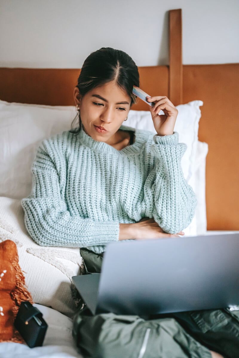 Woman with credit card pondering while buying online with laptop